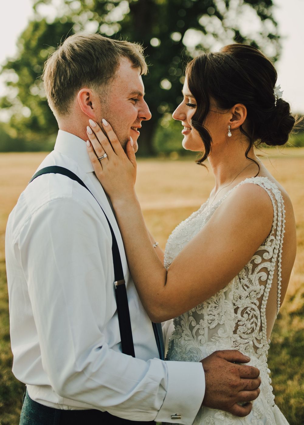 A bride and groom share a romantic moment in a golden field, with the bride gently touching the groom's face.