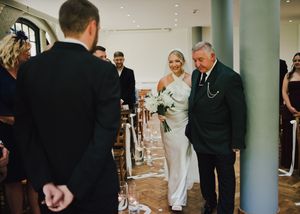 Bride in white gown walks down aisle with older gentleman at elegant wedding ceremony.