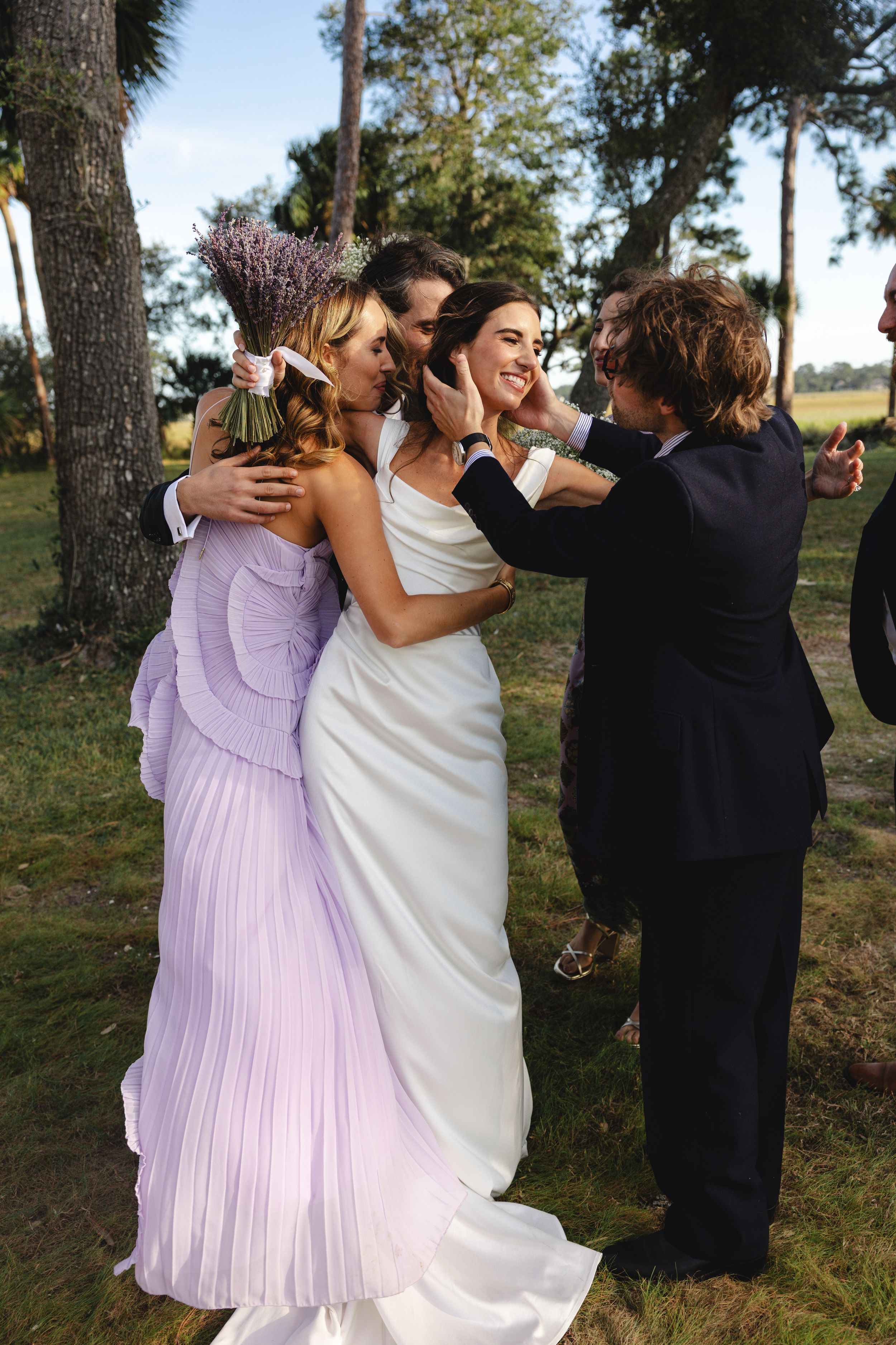 A group of wedding guests in formal attire dancing and celebrating outdoors among trees.