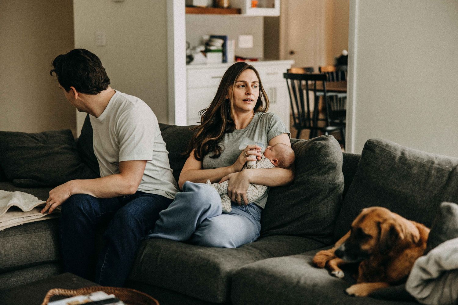 Family relaxing at home on grey couch with sleeping dog.