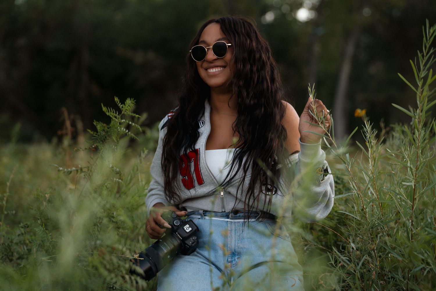 Woman in white top and jeans laughing joyfully in a sunny meadow with wildflowers.