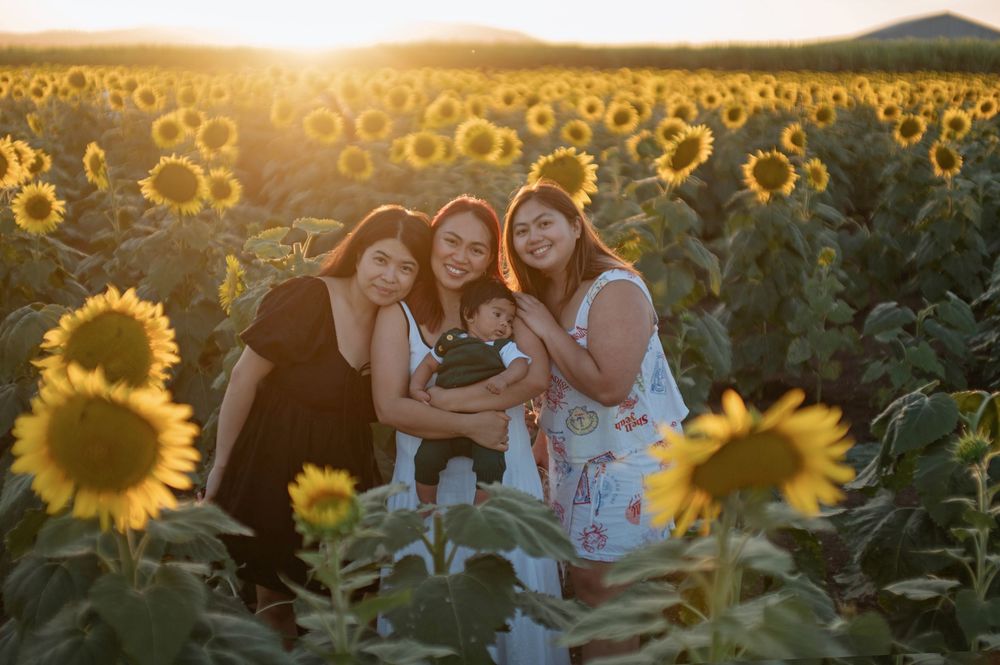 Three women holding a baby in a sunflower field at golden hour sunset.