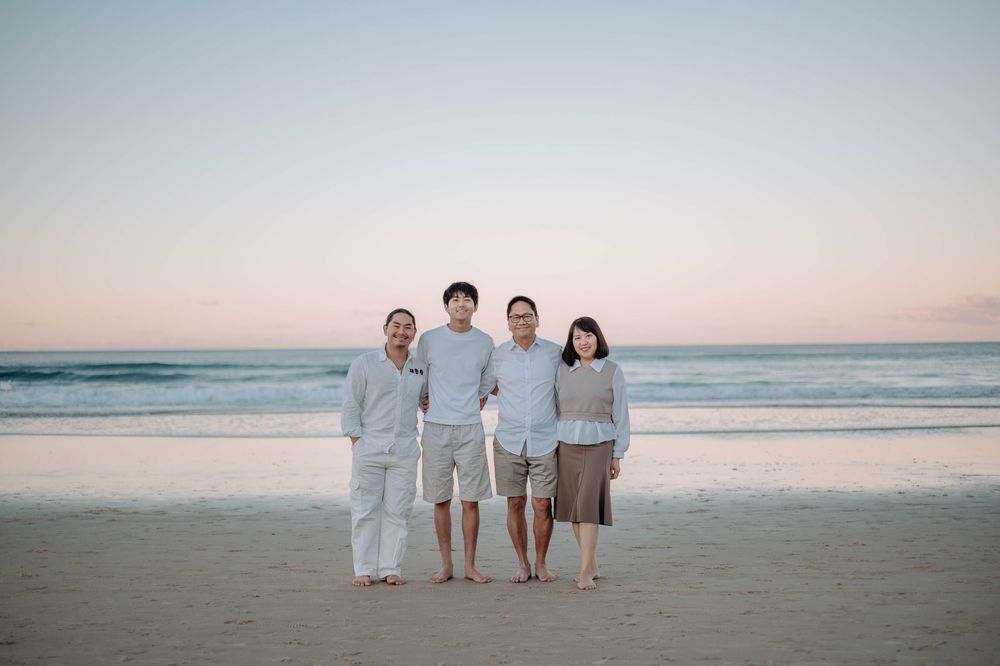 Family of four posing together on a sandy beach at sunset with calm ocean waves in the background.