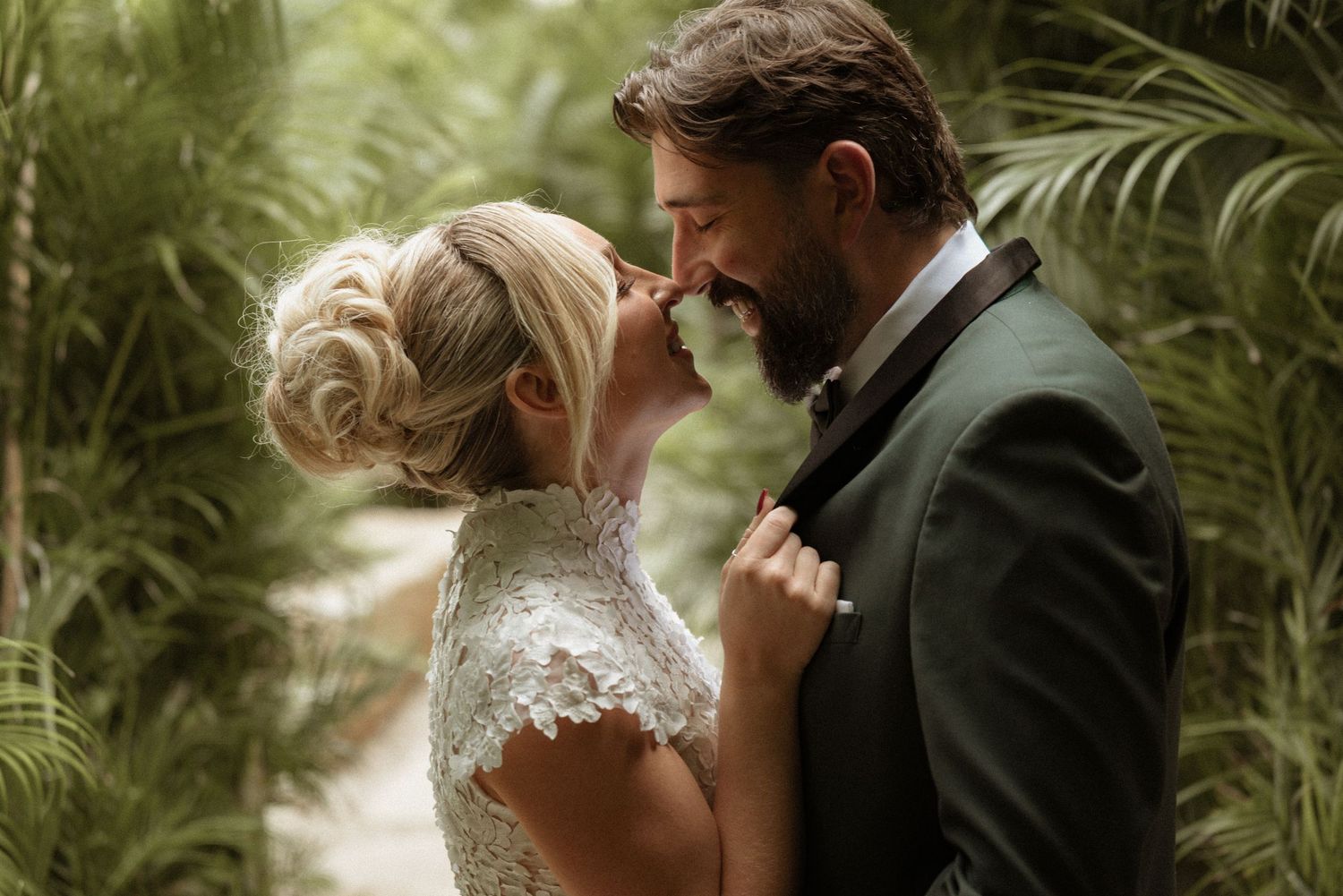 Bride and bearded groom sharing a joyful moment surrounded by lush tropical palm trees.