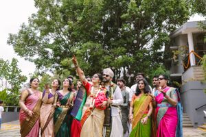 Group photo of wedding attendees in colorful traditional Indian attire under trees outdoors.