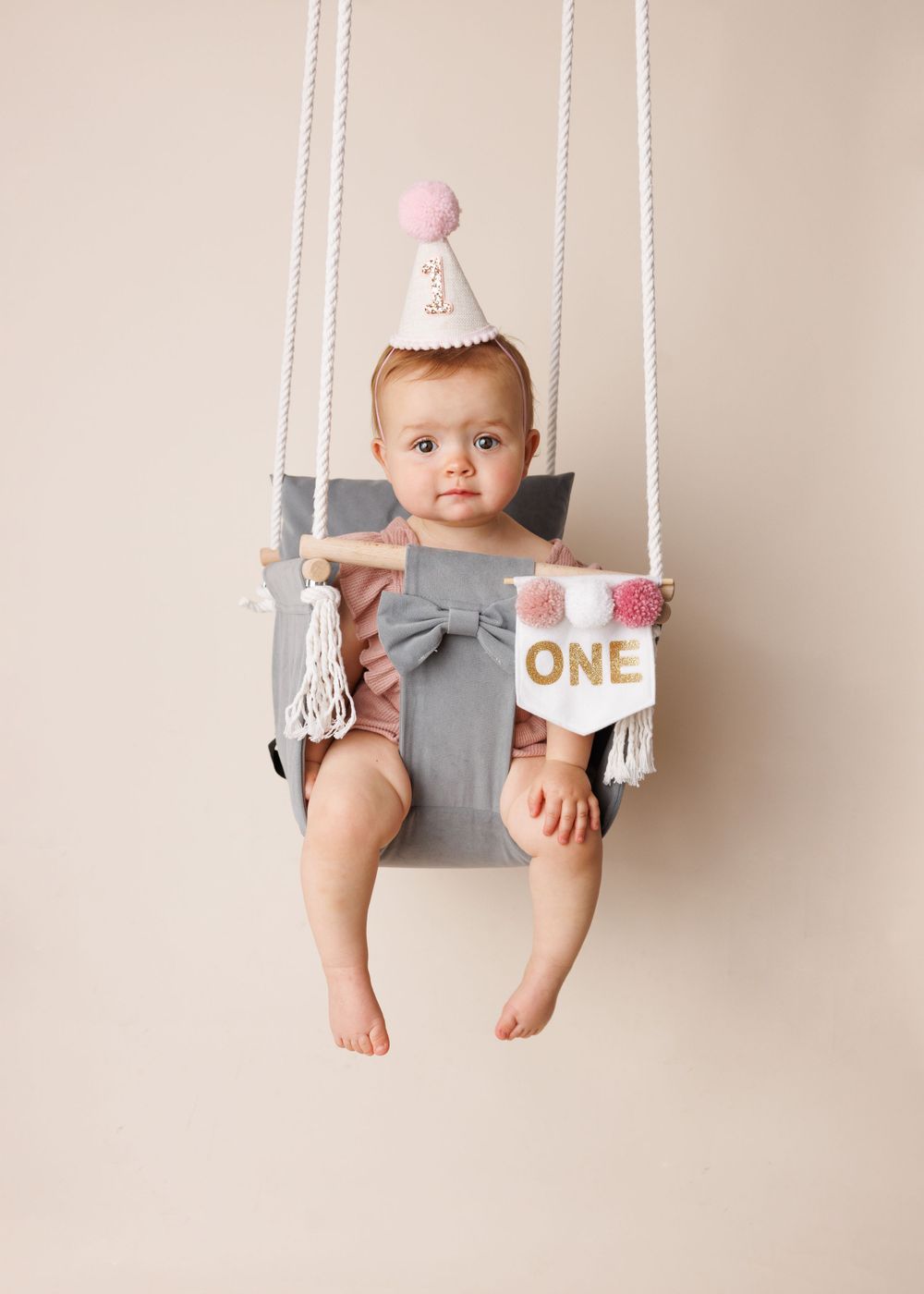 Birthday photo setup with gray swing seat and pink party hat decor.