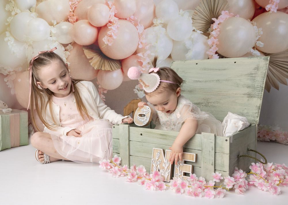 Pink and white balloon arch decorates a whimsical first birthday photoshoot setup with vintage mint green chest.