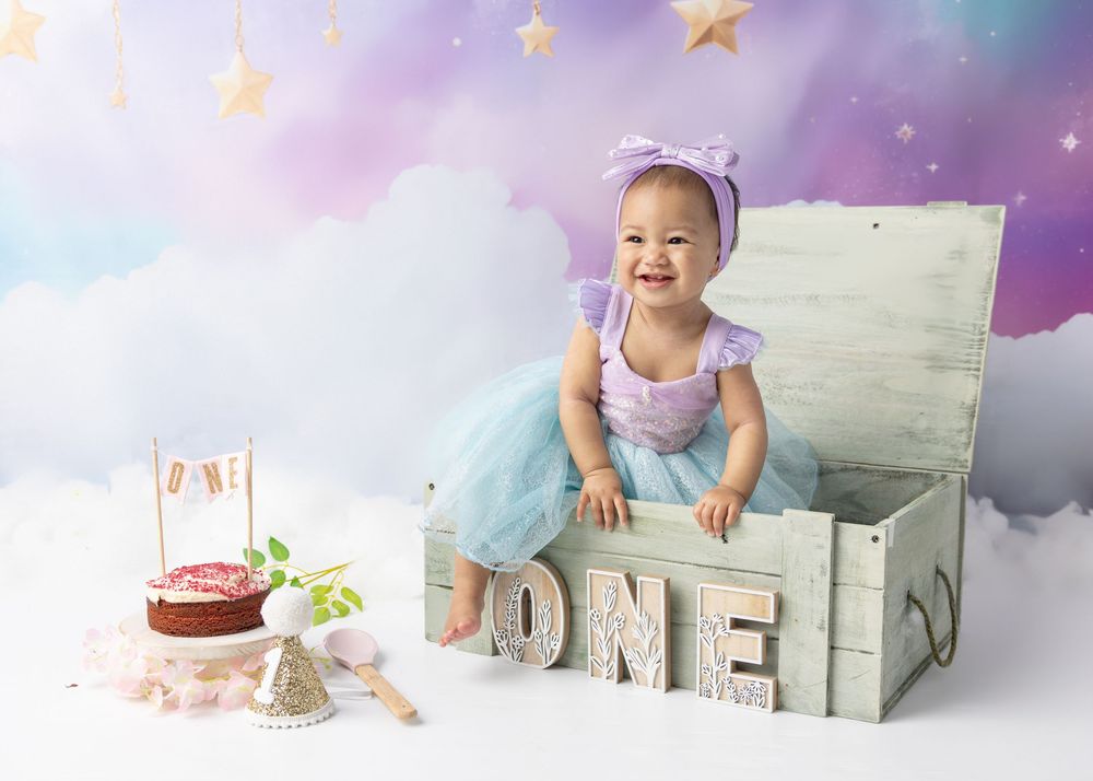 A pink and purple sky backdrop with twinkling stars sets a dreamy scene for a cake smash photo session.