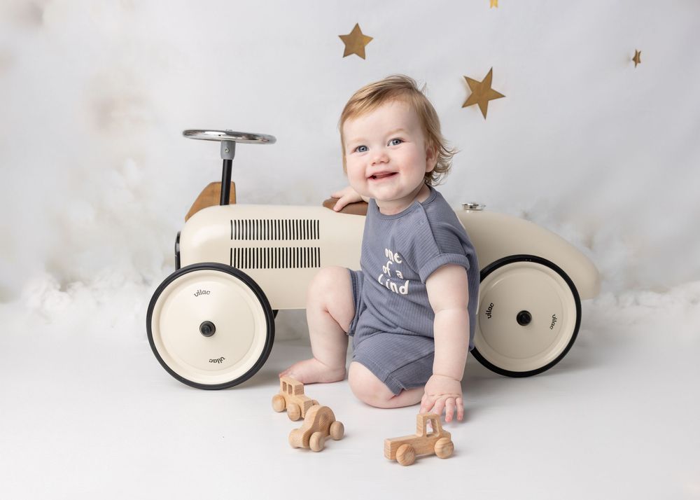 A baby in a grey onesie sits on the floor with gold star decorations and toy bicycle props in a series of photos.