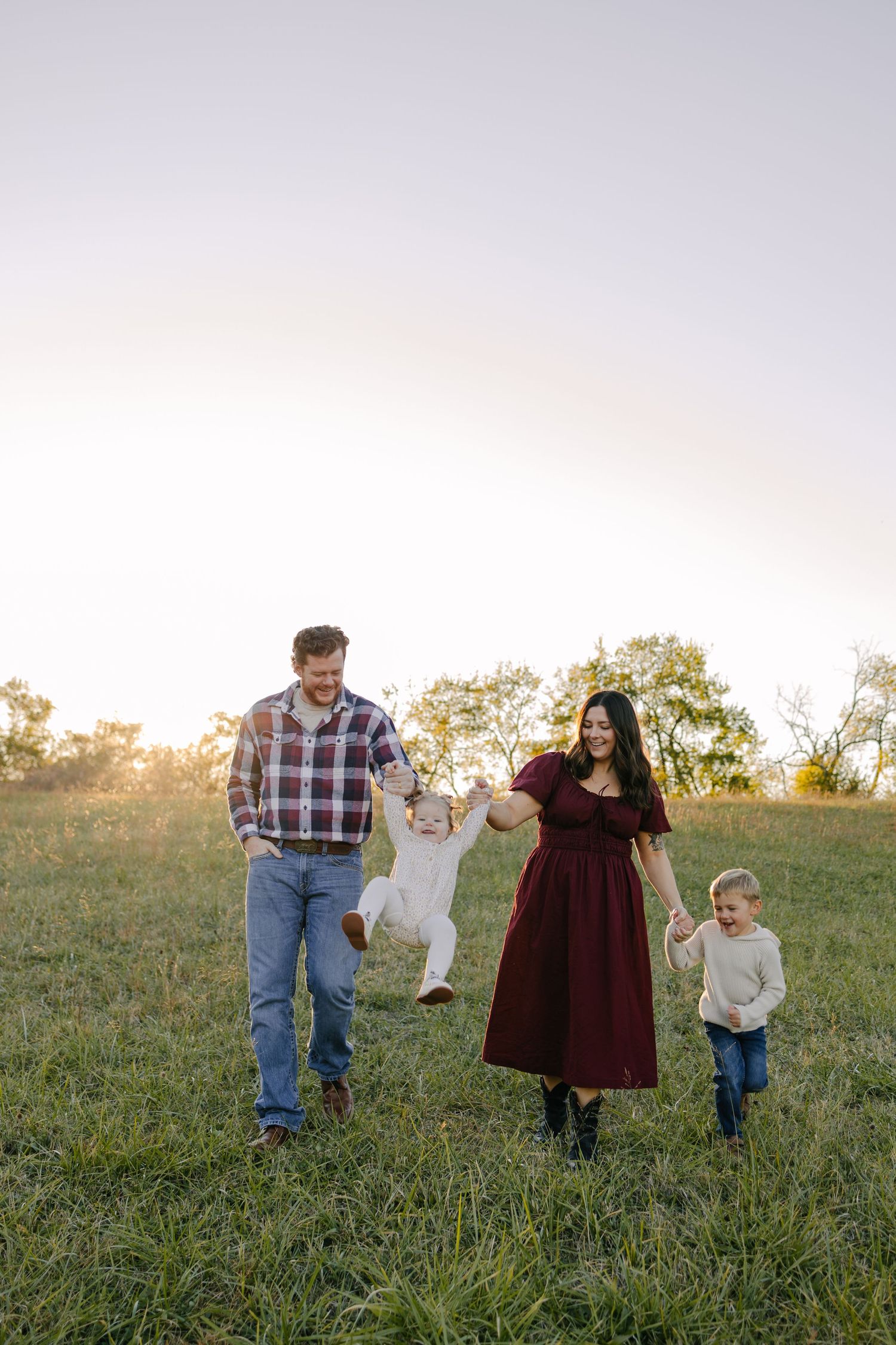 Family photoshoot in rural setting with hay bales and golden field at sunset.