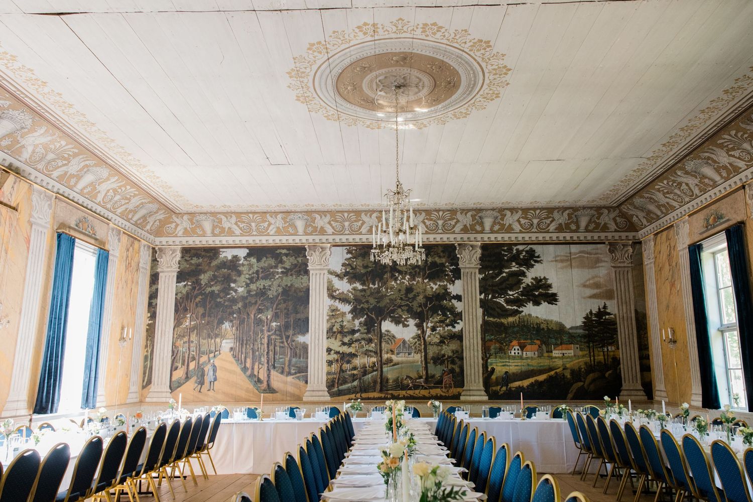 Elegant banquet hall with ornate ceiling, murals, and long tables set for wedding reception.