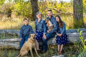 A group enjoying a relaxed autumn photoshoot on a rustic wooden fence with their brown dog against golden foliage.