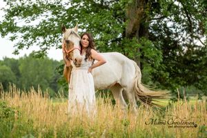 Wedding group poses playfully in lush garden setting wearing romantic white dresses and casual attire.