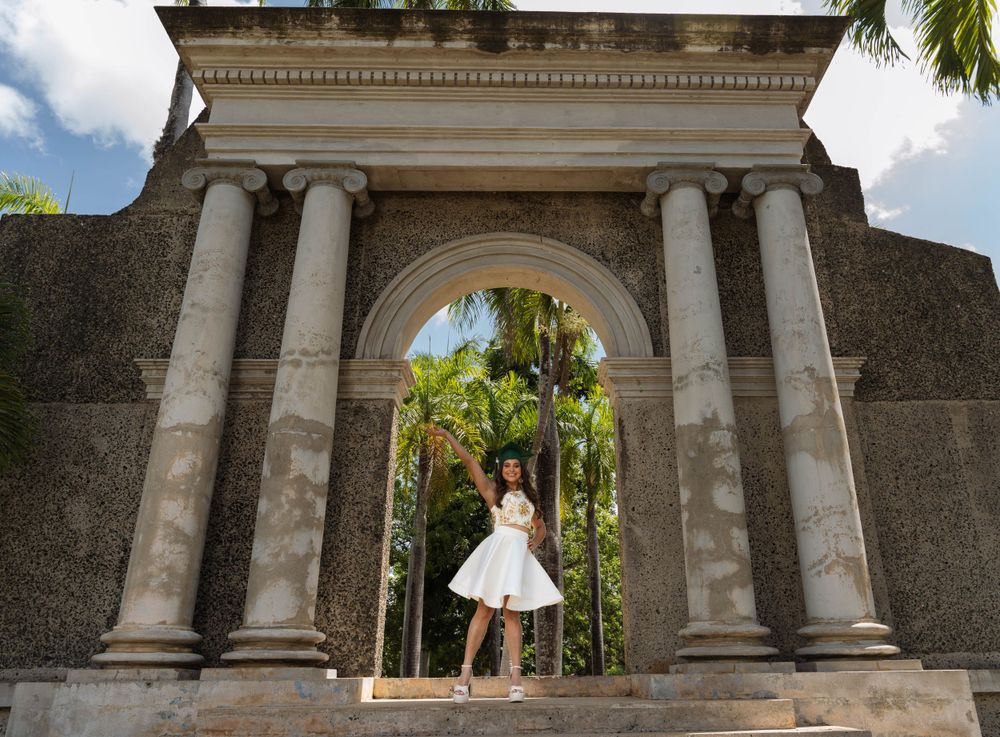 White dress twirling under classical stone archway with palm trees visible.