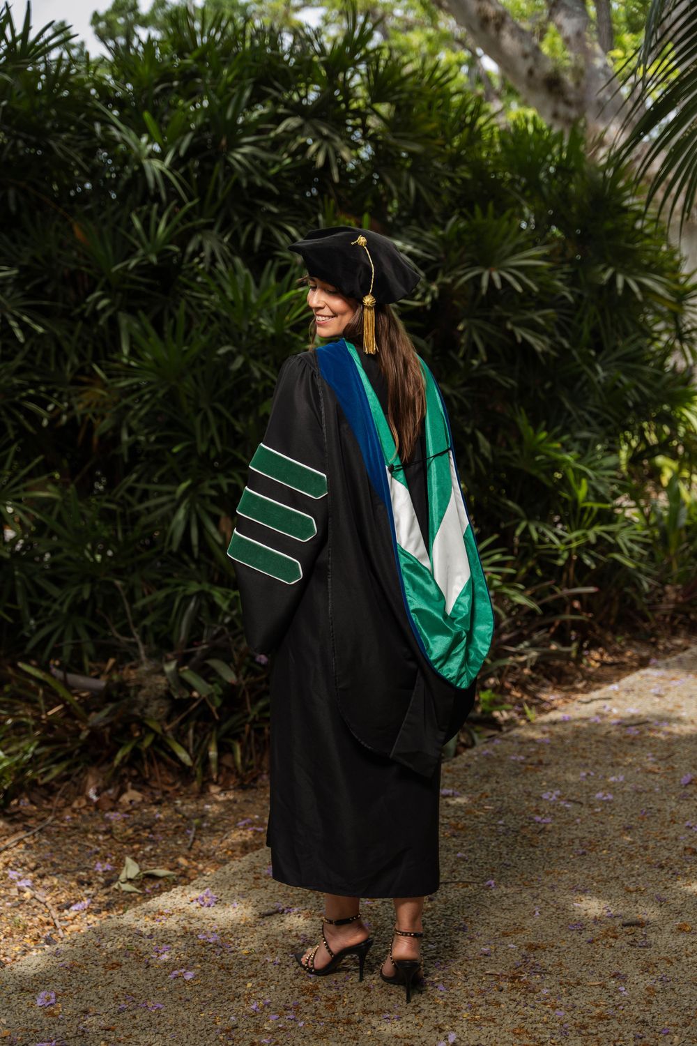 Graduate in academic regalia showing decorative green and black graduation gown from behind.