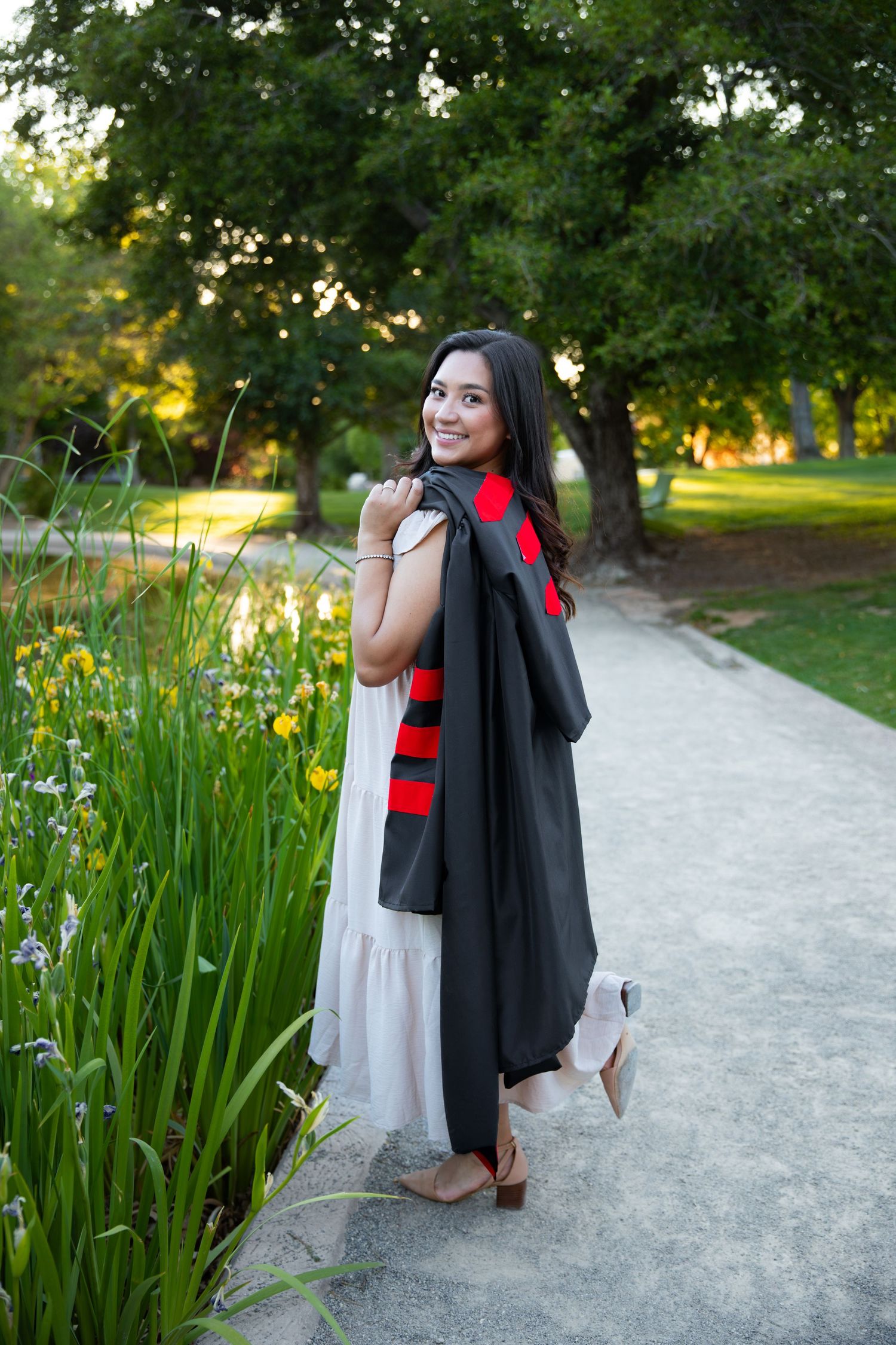 Graduate in red commencement regalia smiles while posing near campus building.