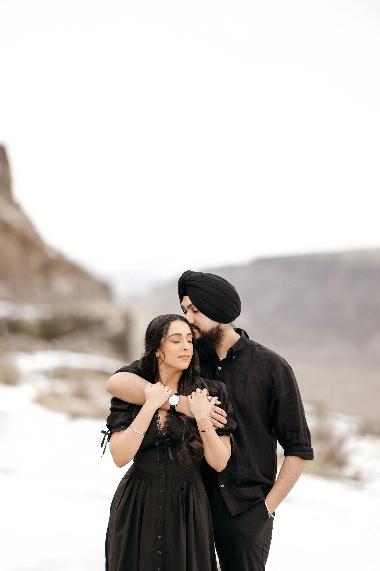 Romantic moment between couple in white outfits on misty beach near cliffs.