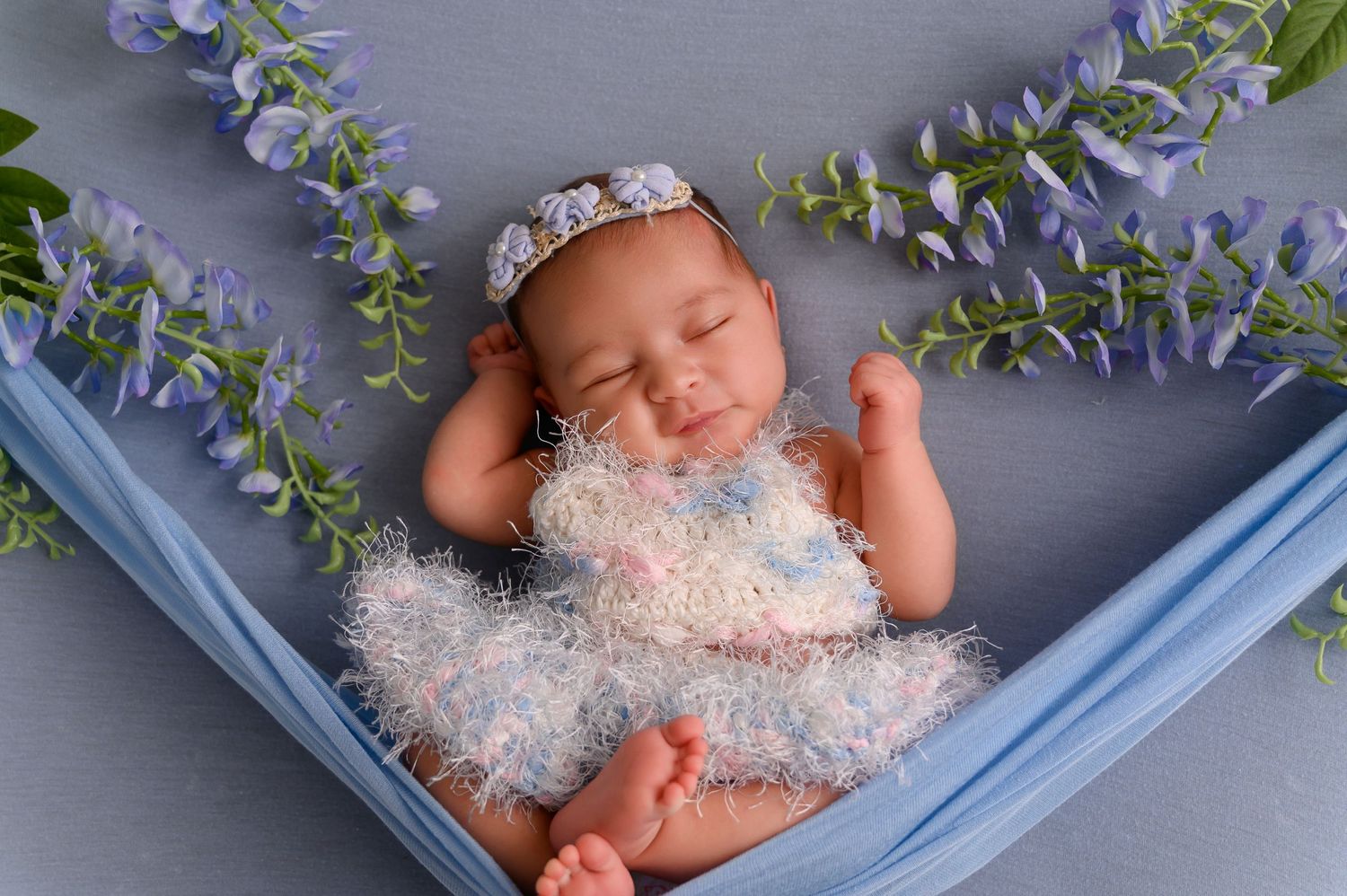 Newborn photography setup with blue frame and delicate flowers against grey backdrop.