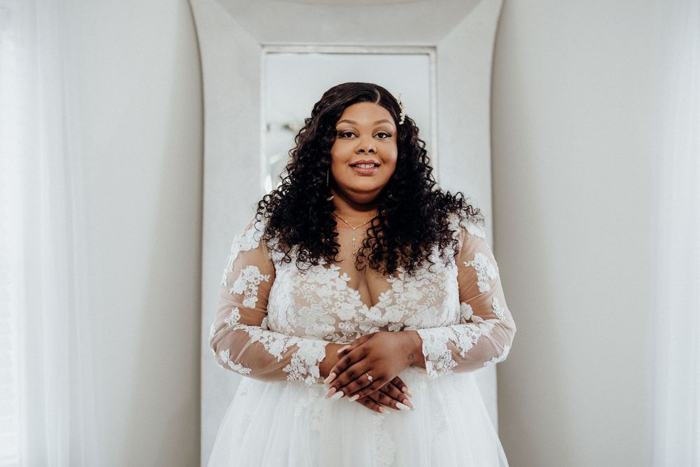 A bride in a beautiful lace wedding gown with long sleeves poses against a white backdrop.