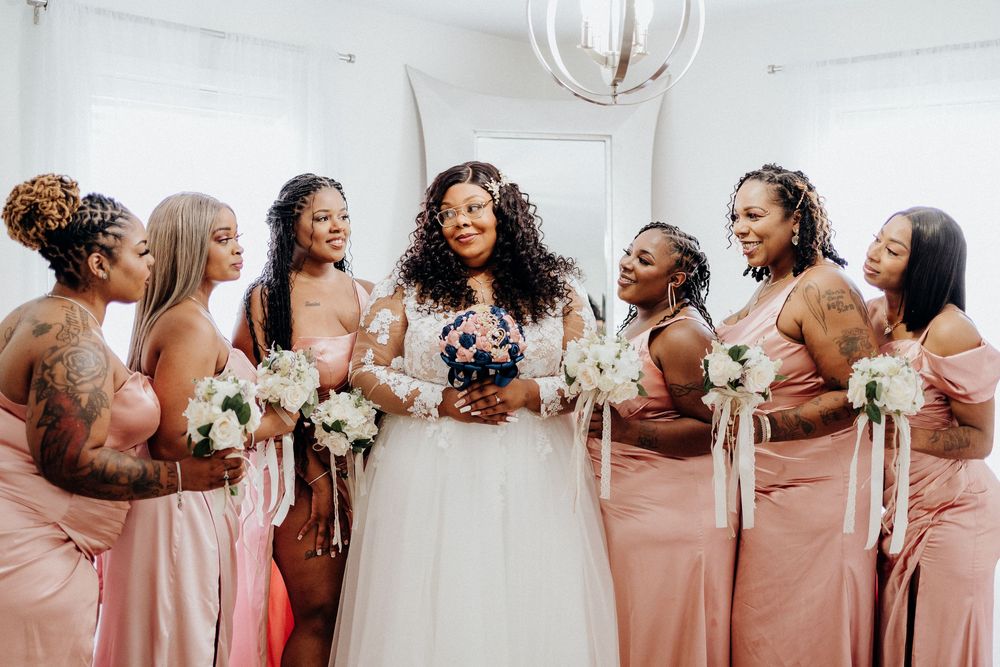 Bridesmaids in blush pink dresses pose together in a line at a wedding celebration.
