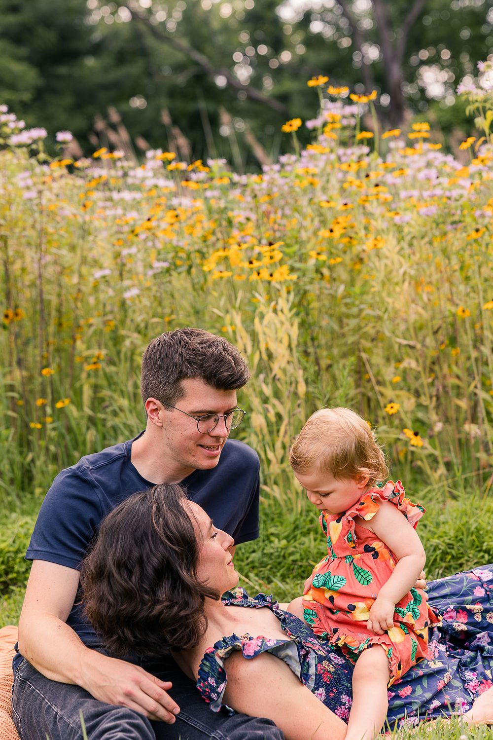 A family relaxes together in a wildflower meadow filled with yellow blooms on a sunny summer day.