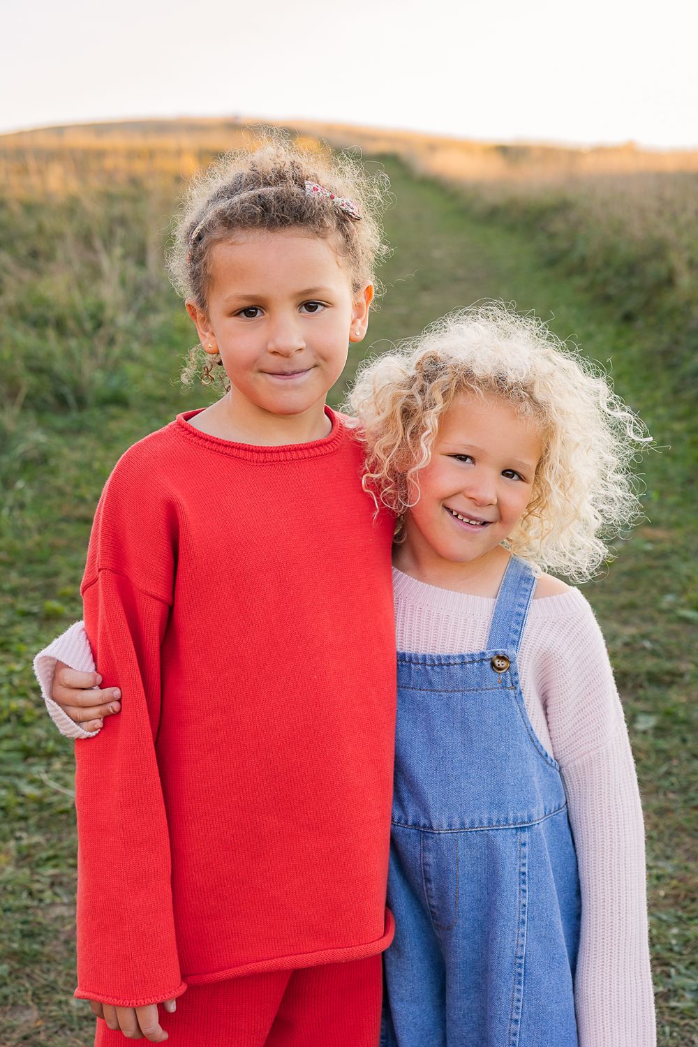 Two children in contrasting red sweater and blue overalls pose together on a grassy path.