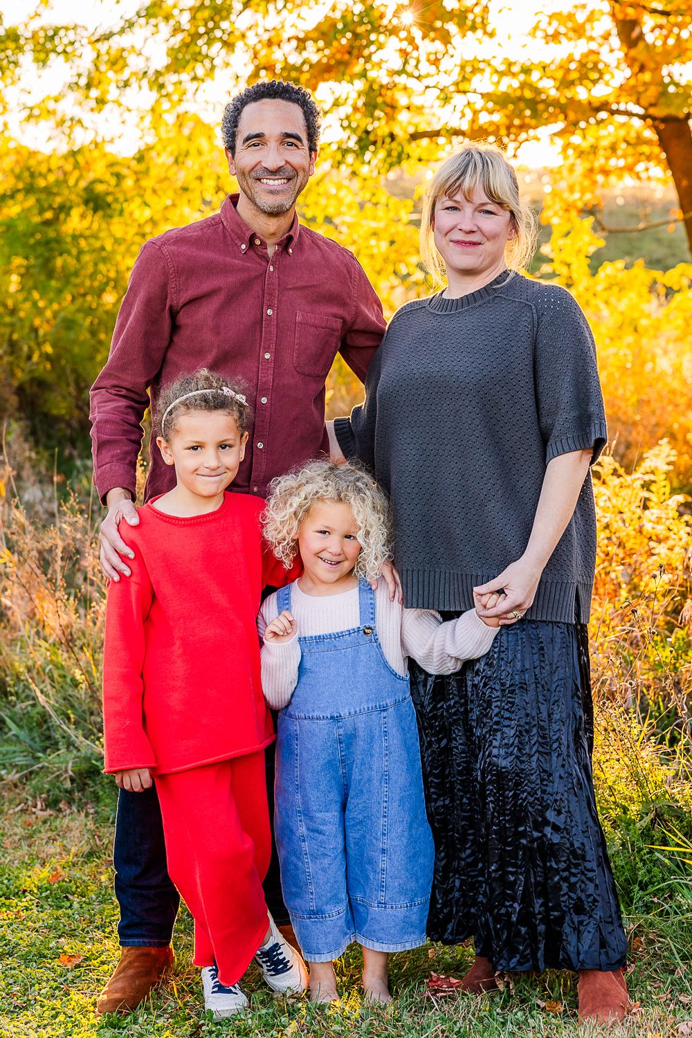 A family of four poses together against autumn foliage during golden hour.