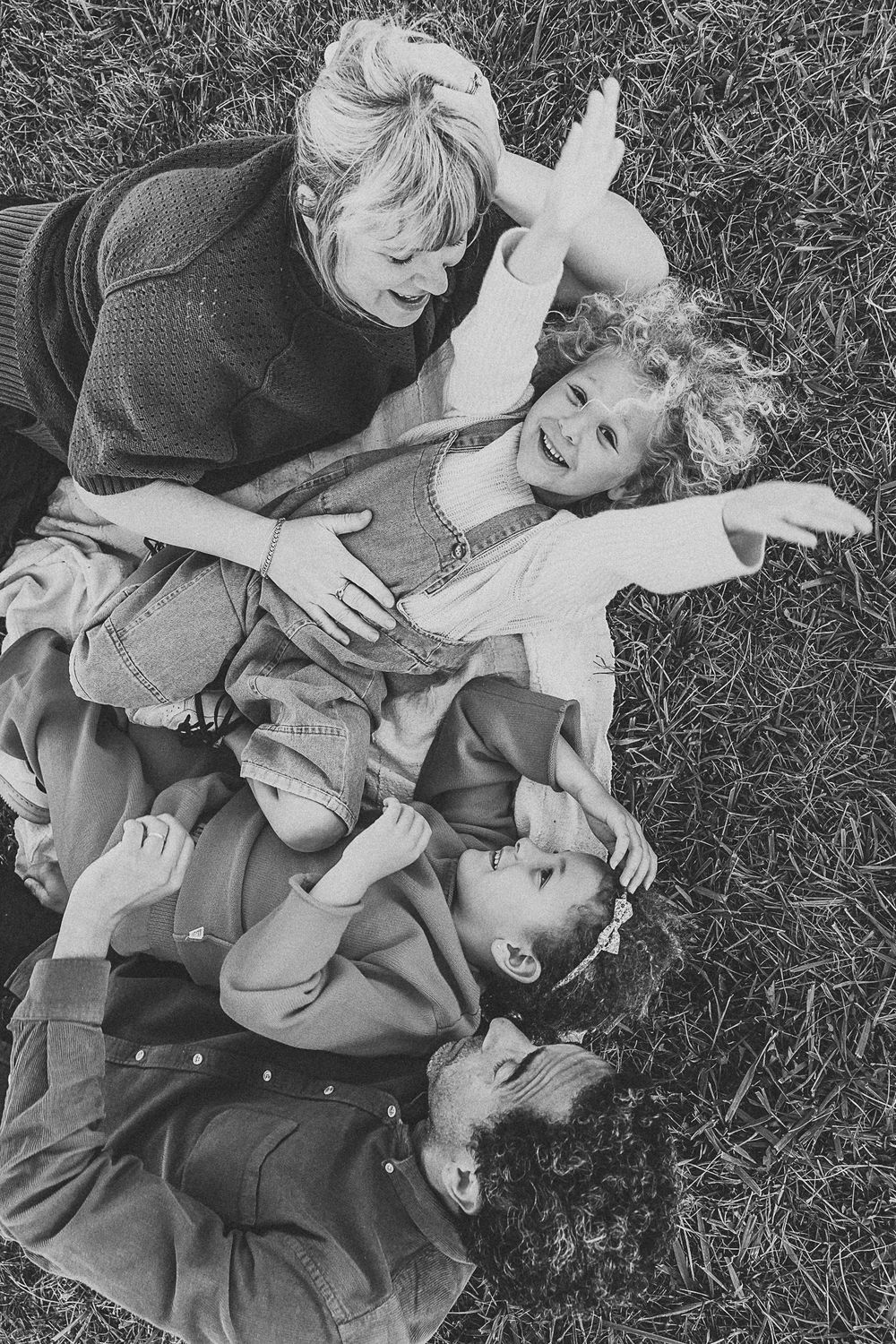 A black and white image of a family lying playfully together on grass.