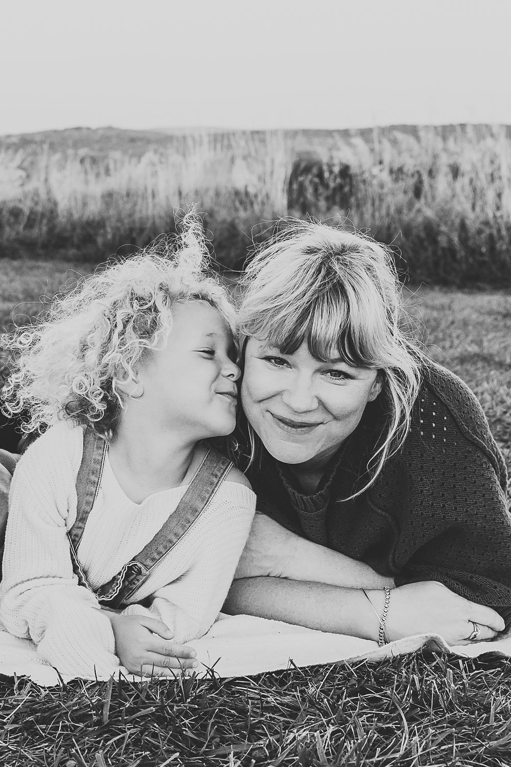 An intimate black and white portrait showing a sweet moment on grassy ground.