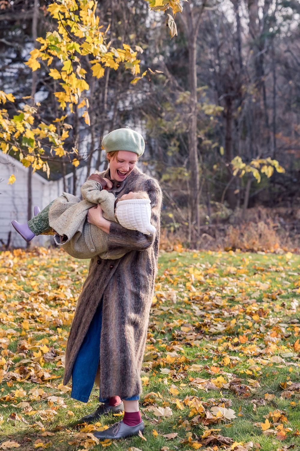 A person wearing a cozy gray coat plays with falling autumn leaves in a park setting on a crisp fall day.