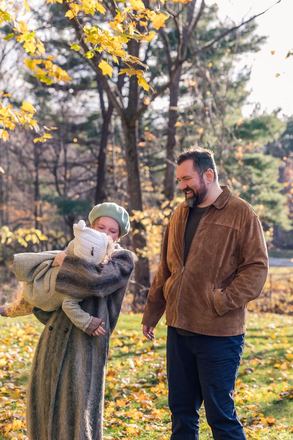 A couple embraces outdoors on an autumn day with golden leaves and pine trees in the background.