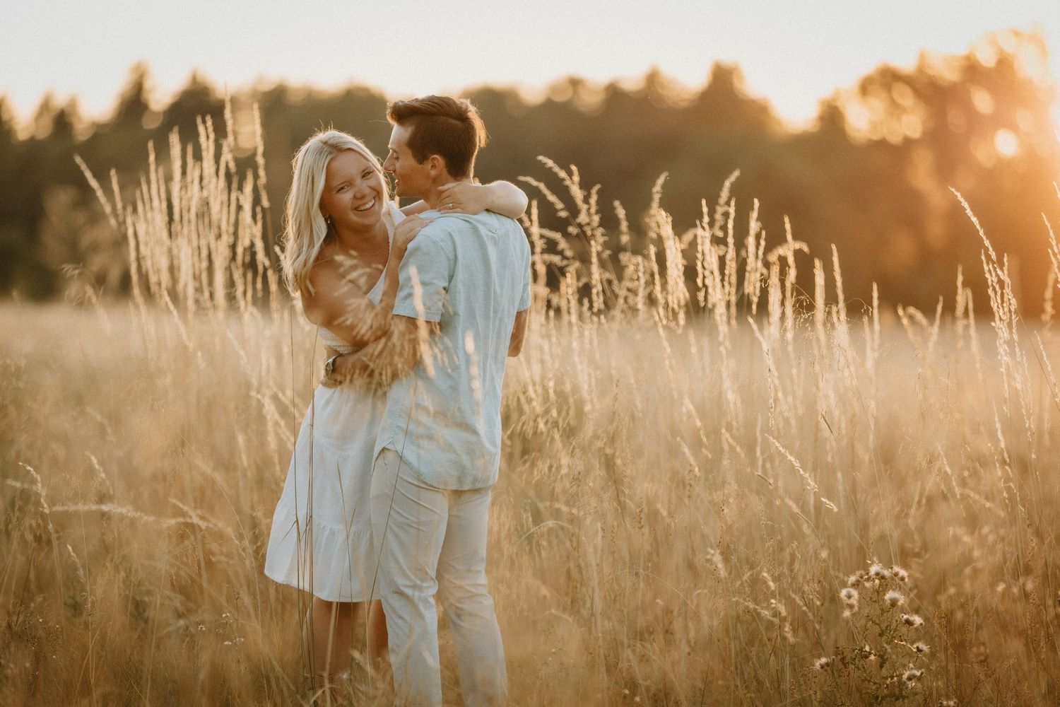 A couple embraces in a golden wheat field during sunset, backlit by warm summer evening light. Chehalem, Oregon