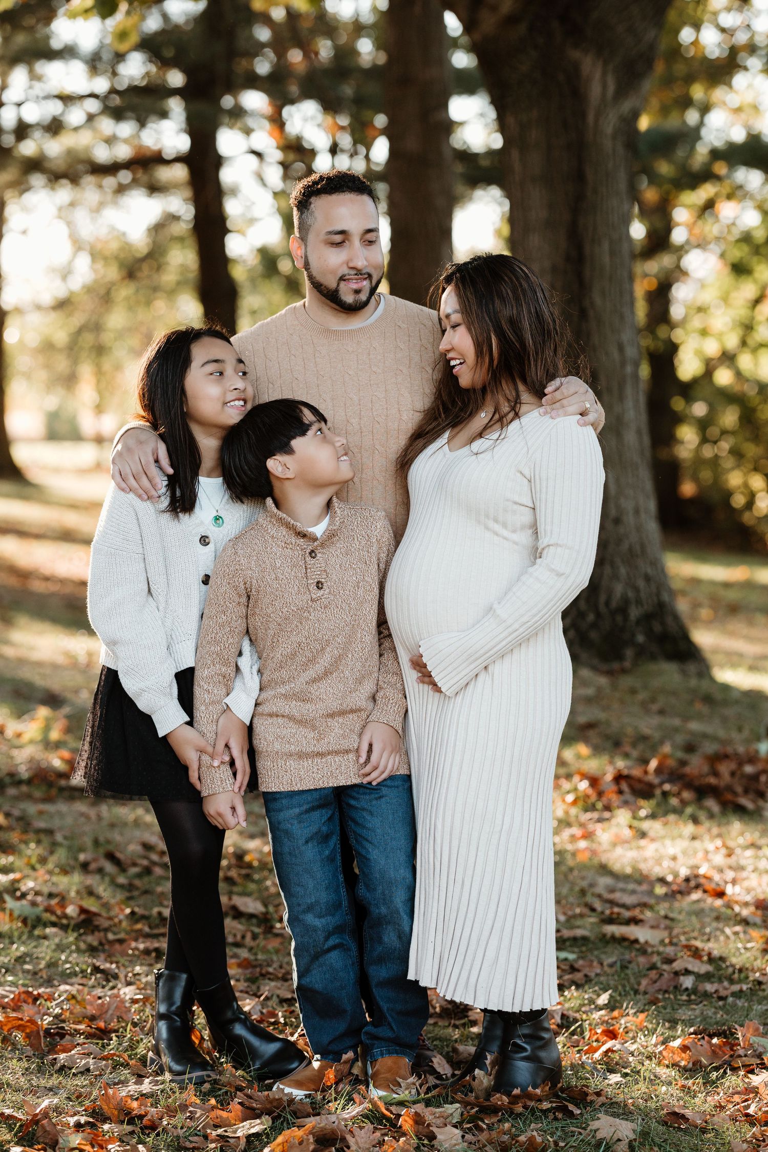 Family of four standing together among autumn trees in warm sweaters.