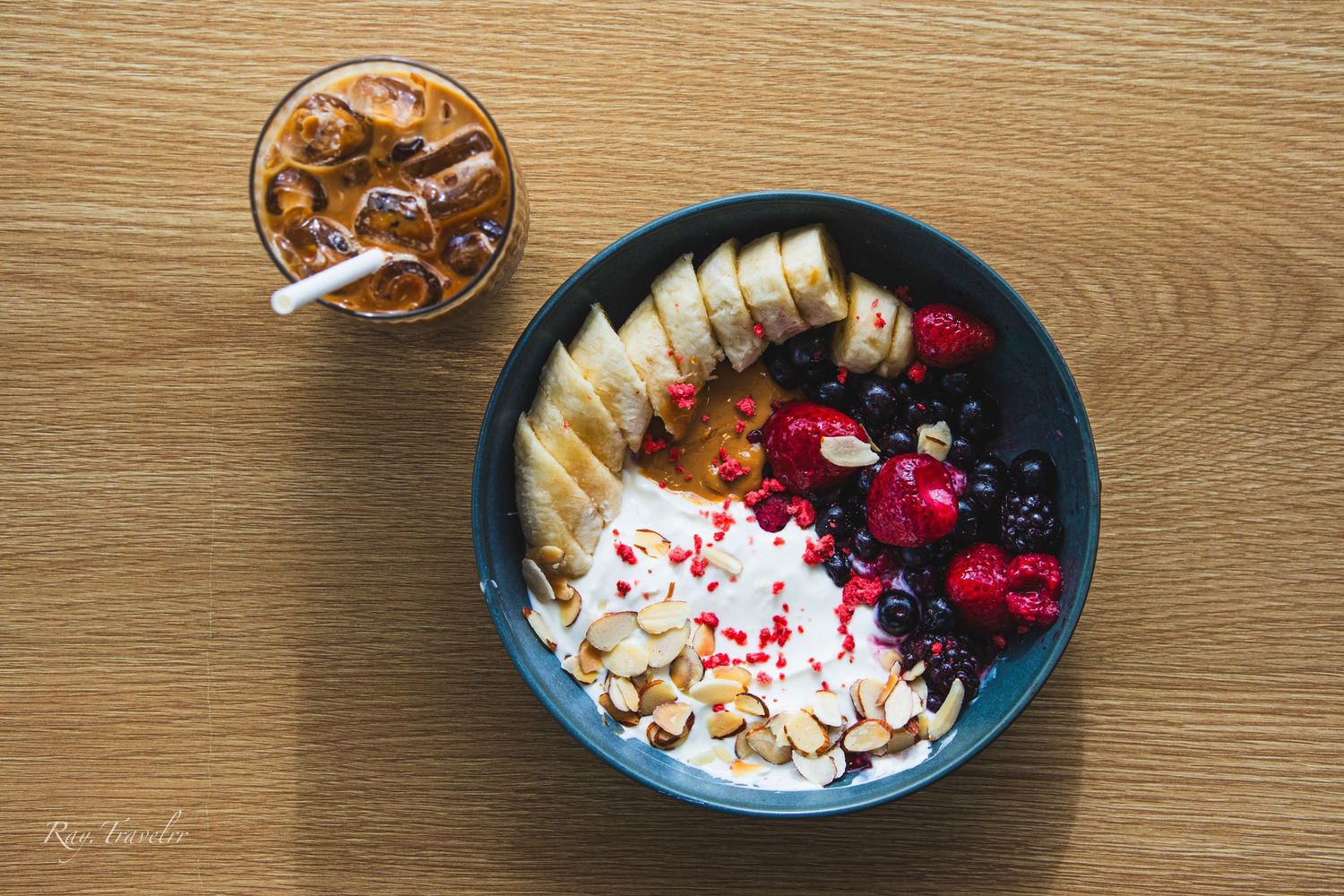 Top-down shot of breakfast bowl with fresh fruit and nuts paired with iced coffee.