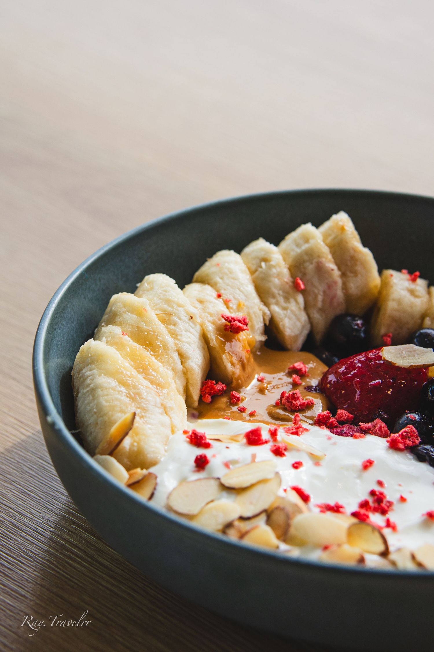 Close-up of artistic breakfast bowl featuring sliced bananas, berries and yogurt garnish.