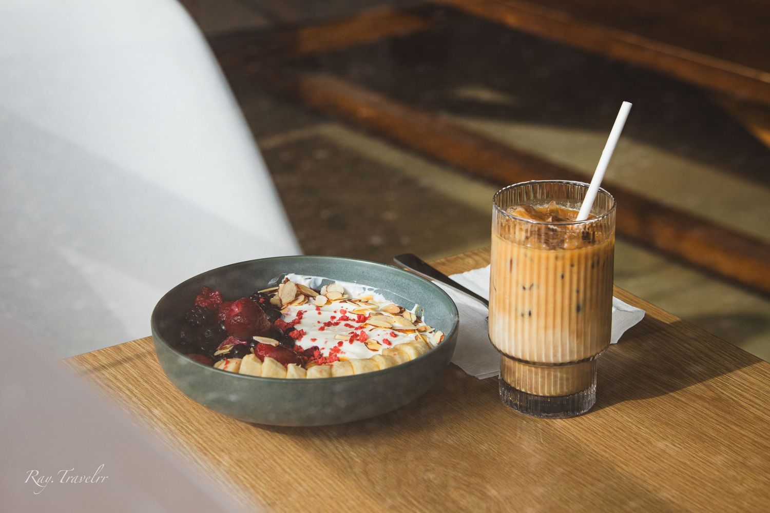 Artisanal breakfast bowl with fresh fruit and nuts served with iced coffee on wooden surface.