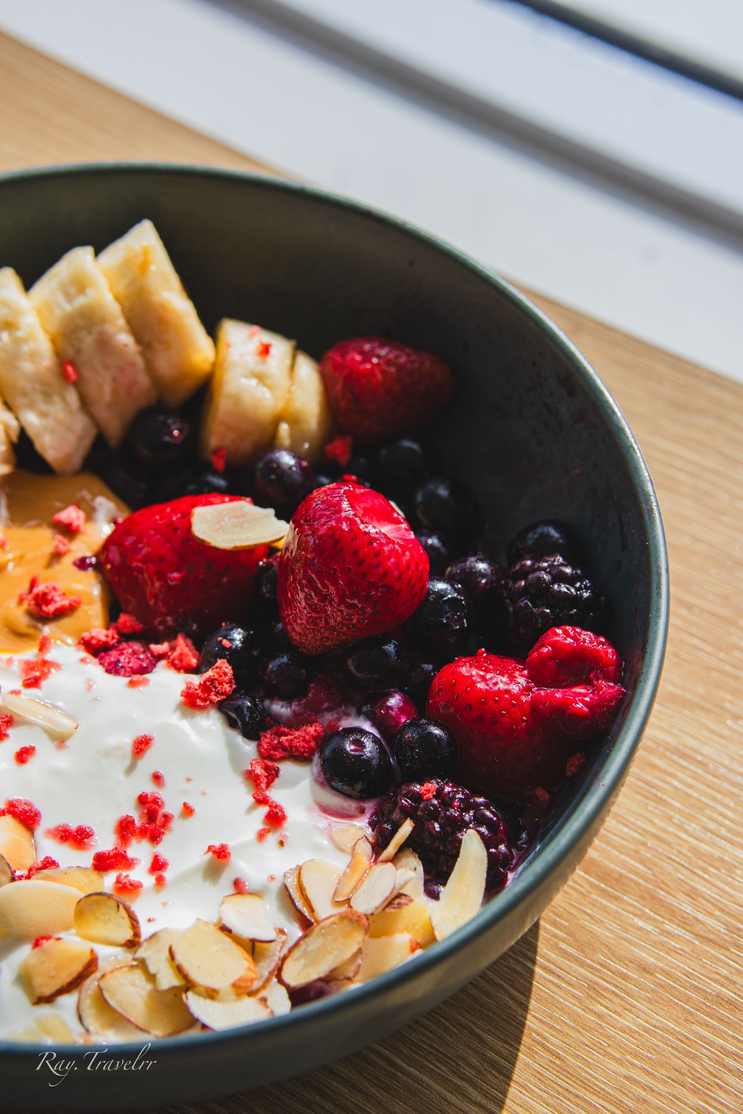 Fresh fruit bowl with berries, sliced bananas, and almonds topped with yogurt and red sprinkles.