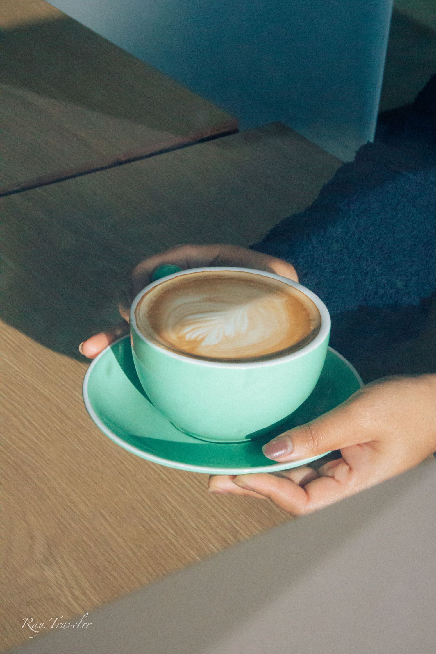 A mint green cup filled with latte art on a wooden table.