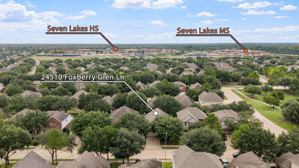 Aerial view of residential homes in a suburban neighborhood on a sunny day with scattered clouds overhead.