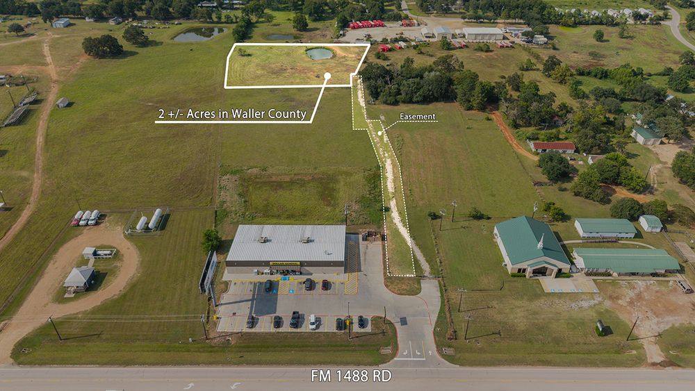 Aerial drone footage shows overhead view of residential properties with green lawns and buildings in rural area.
