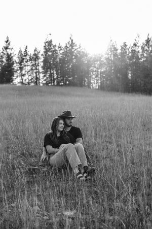 Black and white photo of couple relaxing in tall grass field near forest.