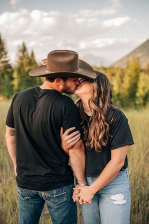Couple in matching black shirts share an intimate moment in a mountain meadow at sunset.