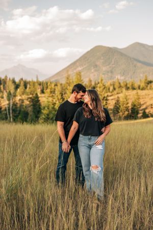 Couple in casual attire sharing a tender moment in a mountain meadow with evergreen trees.