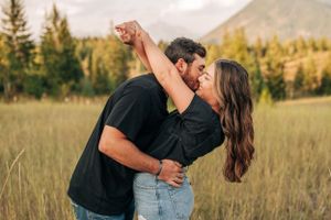 Romantic couple dancing in a mountain field during sunset with pine trees in background.