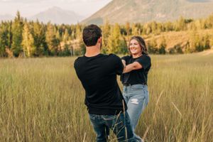 Couple dancing in a mountain meadow with evergreen forest and mountains in background.