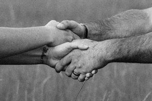 Black and white close-up of two people's hands clasped together in a handshake.