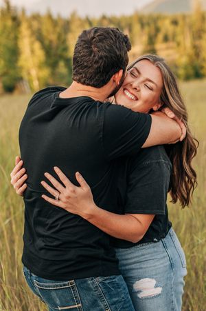 Couple embracing and laughing in a mountain field during golden hour.