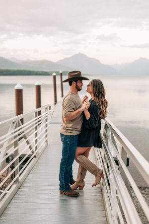 Couple sharing romantic moment on pier railing with misty mountain lake in background.