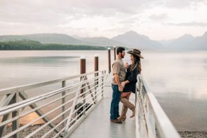 Couple embracing on wooden pier with scenic mountain lake vista behind them.