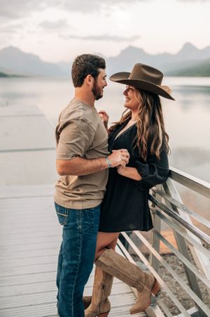A romantic couple shares an intimate moment on a dock overlooking a mountain lake at sunset.